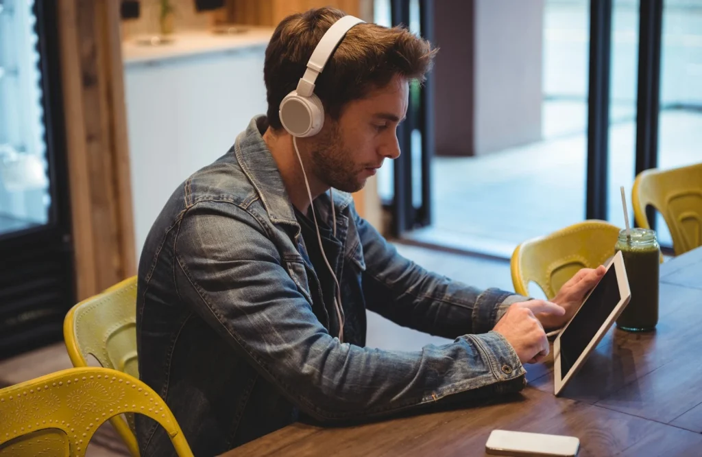 Man headphones using a tablet at a cafe table. He appears focused and relaxed
