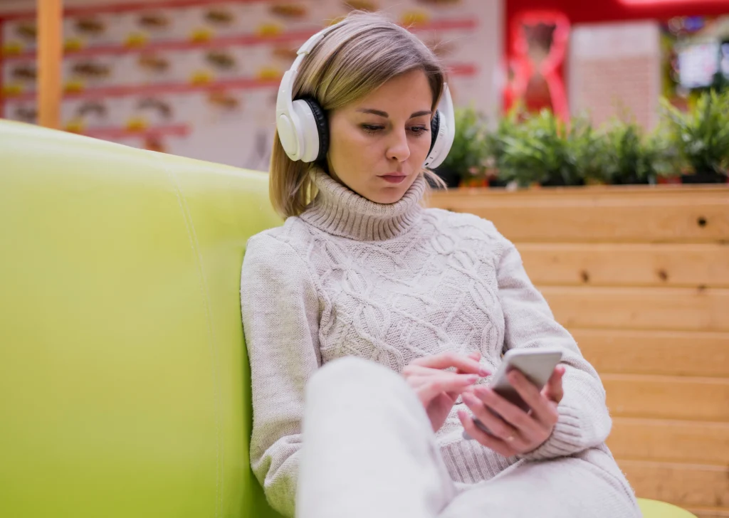 woman-wearing-headphones-sitting-couch-looking-phone